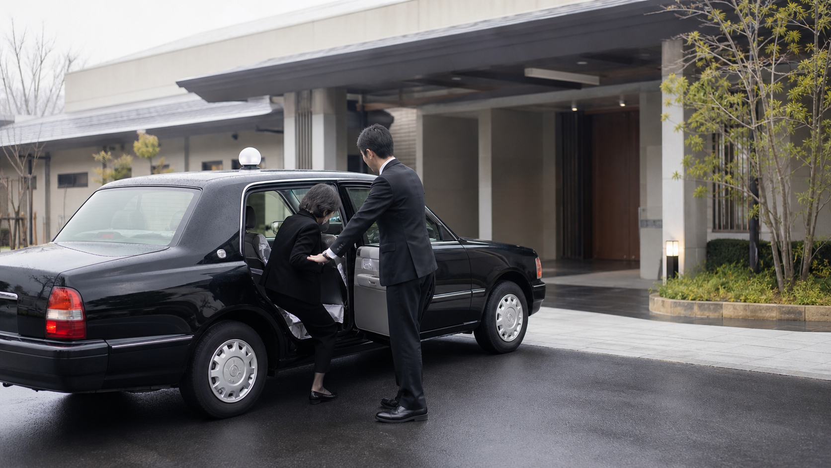 葬儀会館前で高齢の参列者を降ろす送迎車